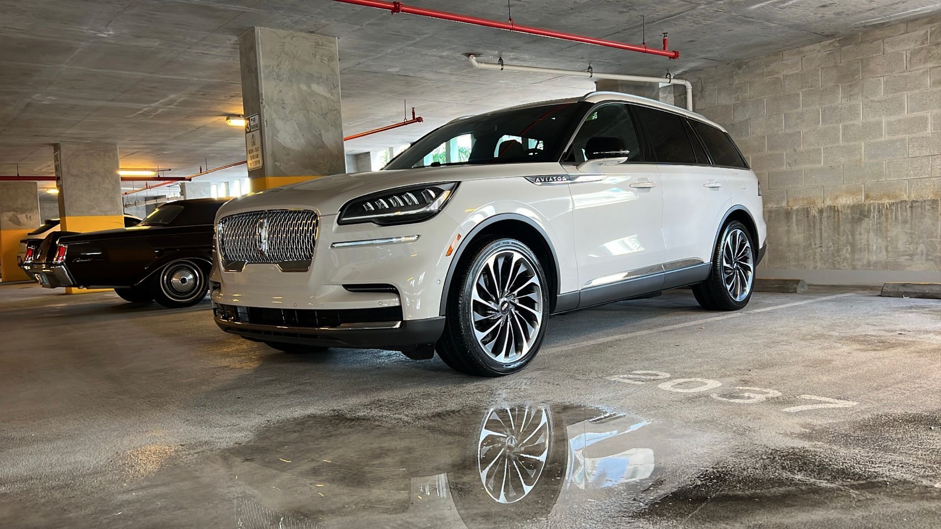 A white suv is parked in a parking garage next to a black suv.