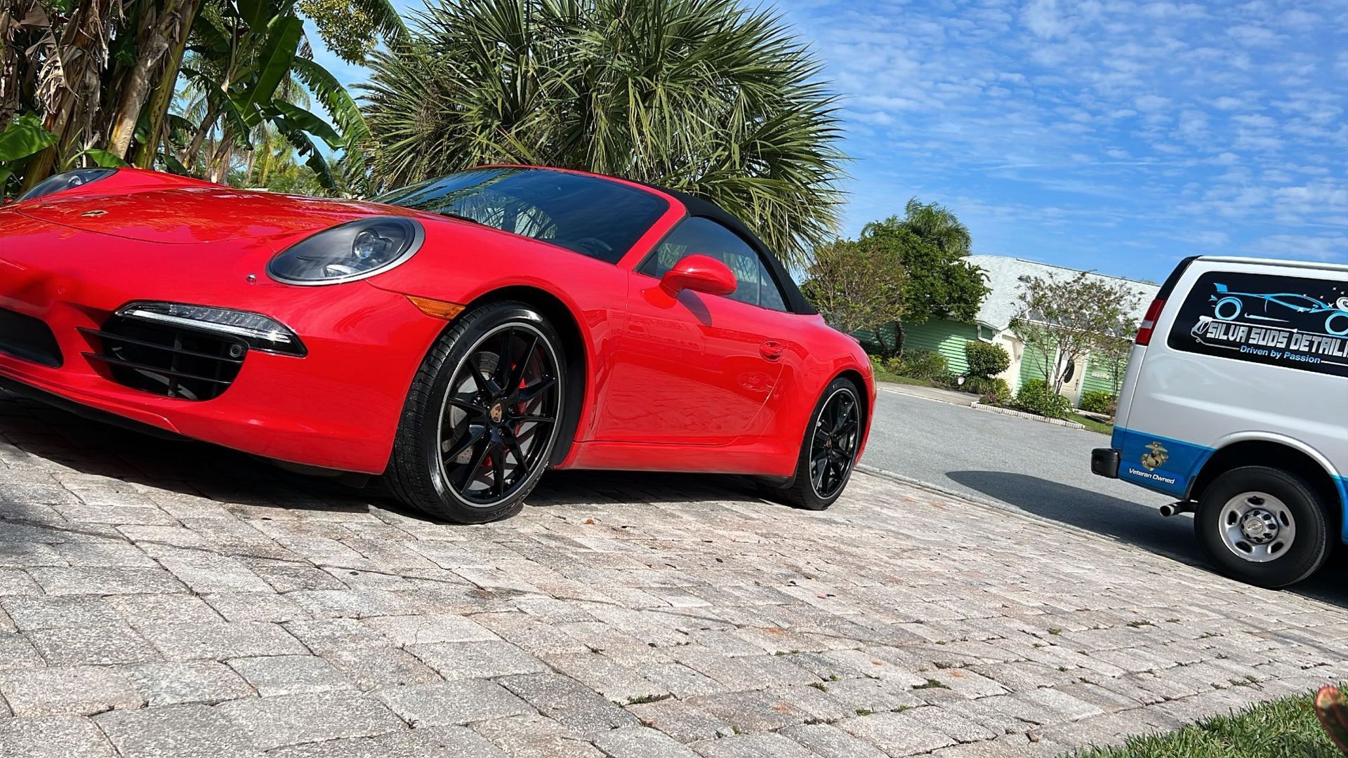 A red sports car is parked on the side of the road next to a white van.