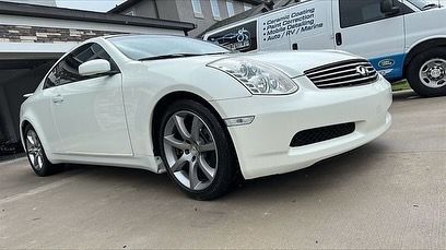 A white car is parked in a driveway next to a van.