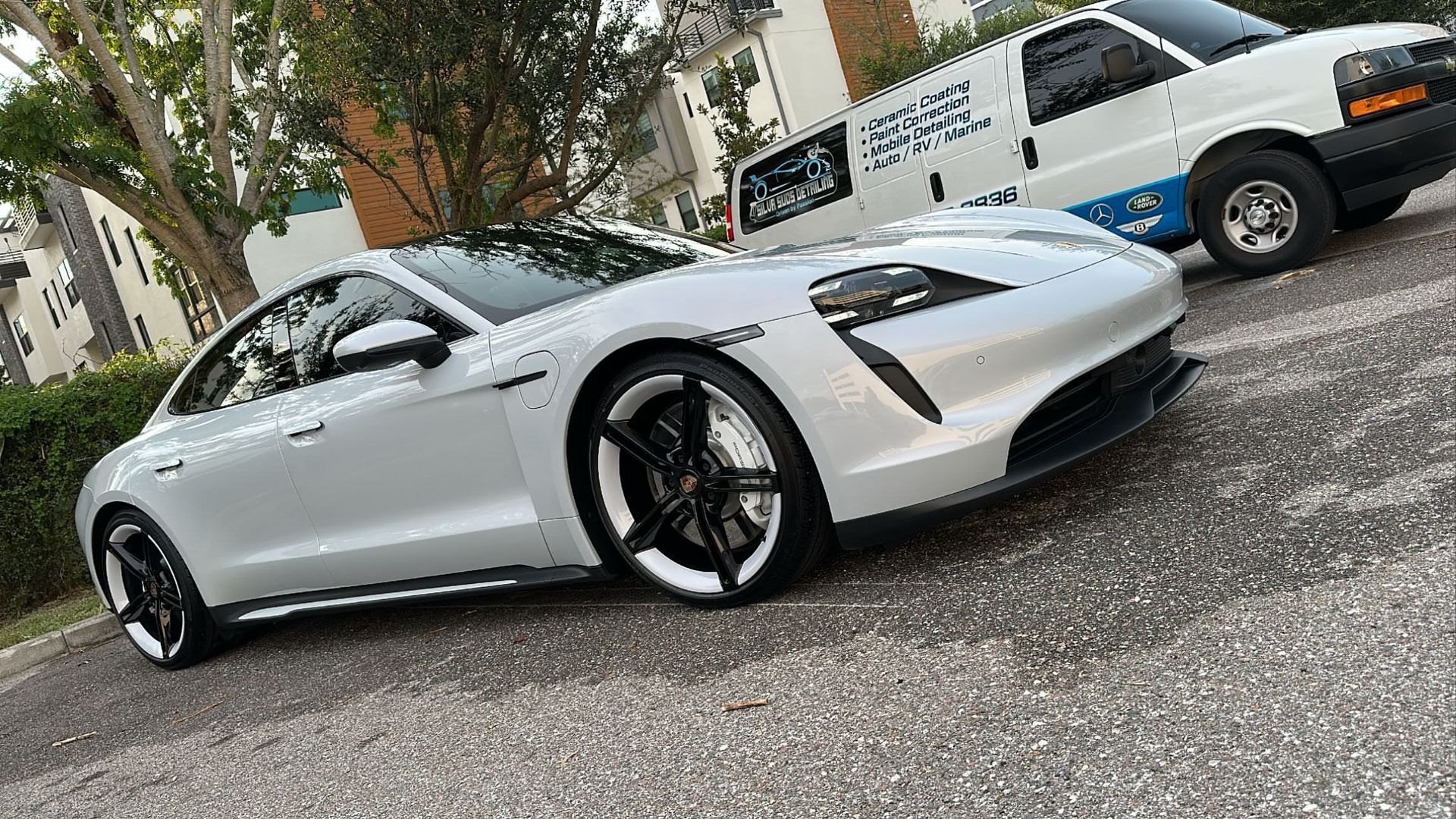 A white porsche taycan is parked next to a white van.