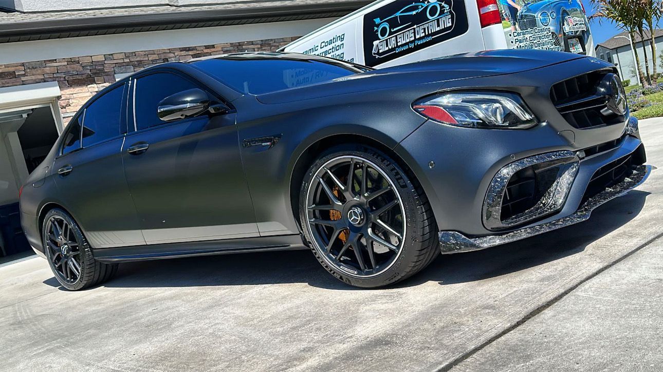A black mercedes benz is parked in a driveway in front of a building.