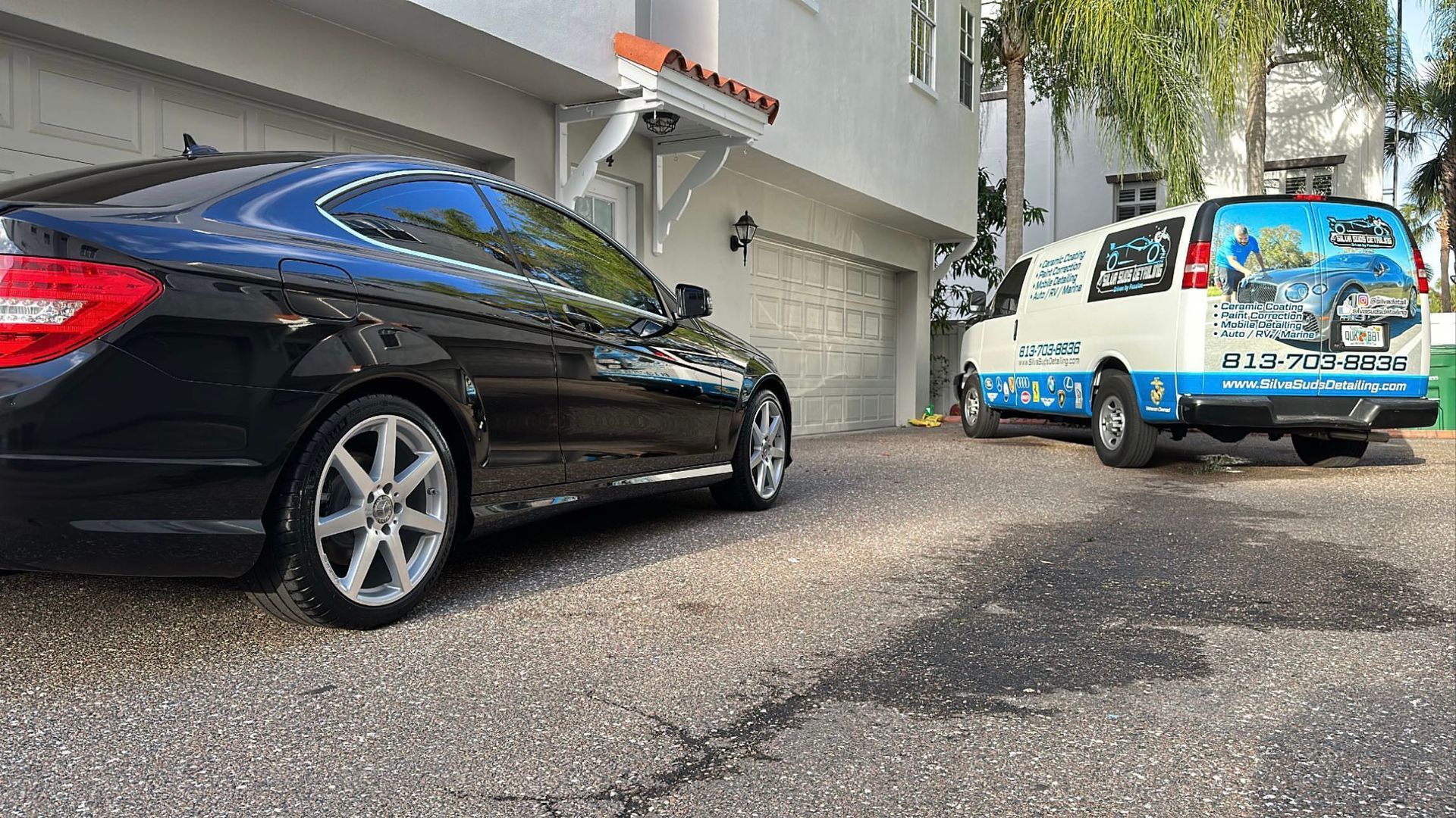 A black car and a white van are parked in front of a garage.