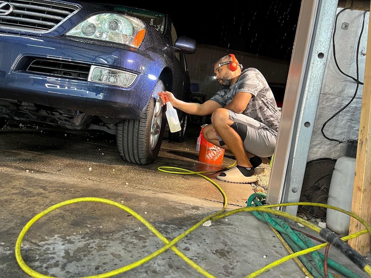 A man is kneeling down to wash a car in a garage.