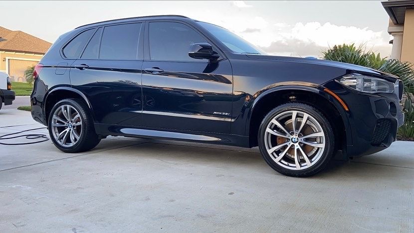 A black bmw x5 is parked in a driveway next to a house.
