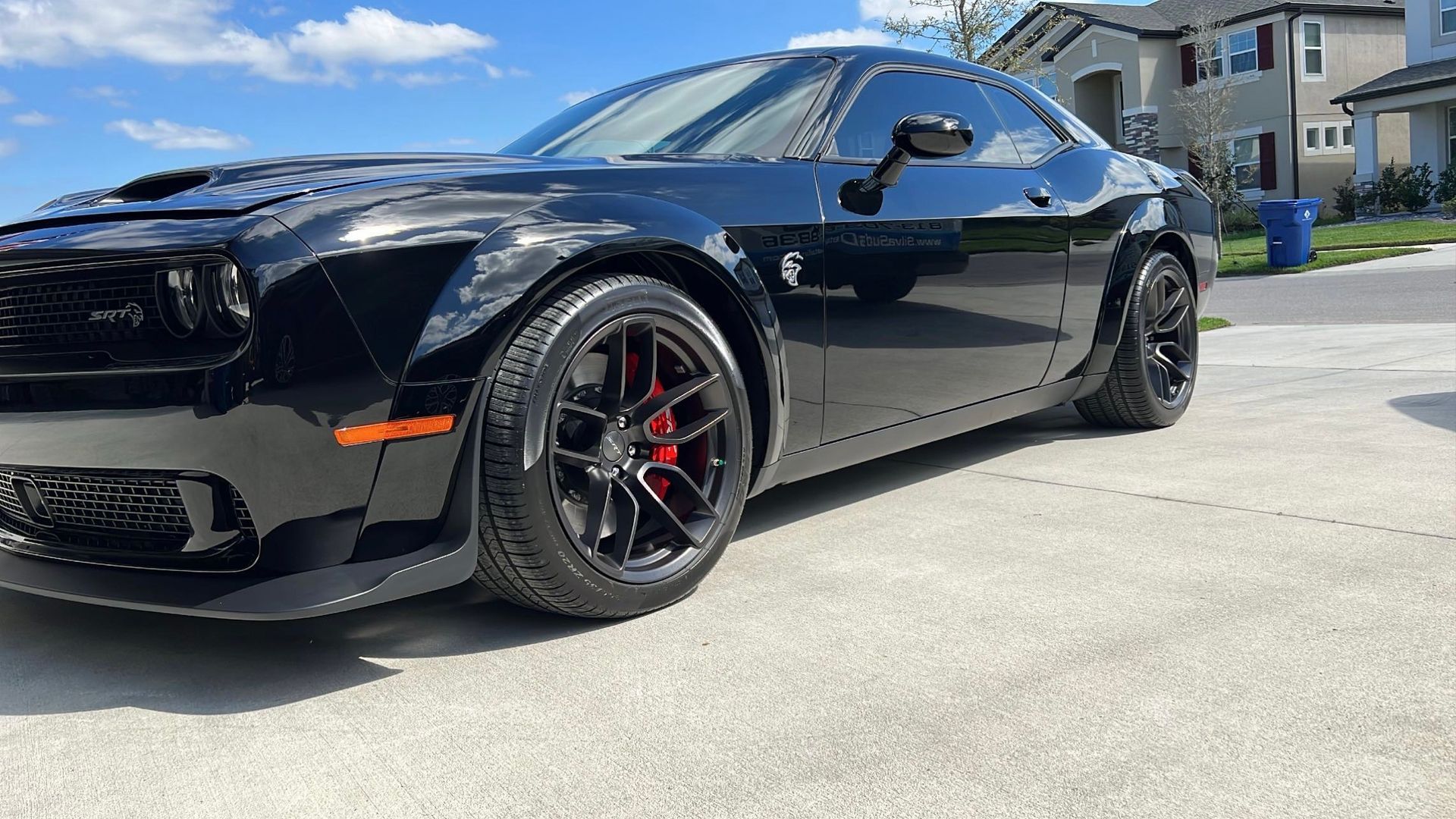 A black dodge challenger is parked in a driveway in front of a house.