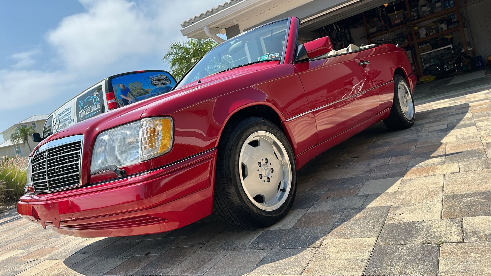 A red mercedes benz convertible is parked in front of a house.