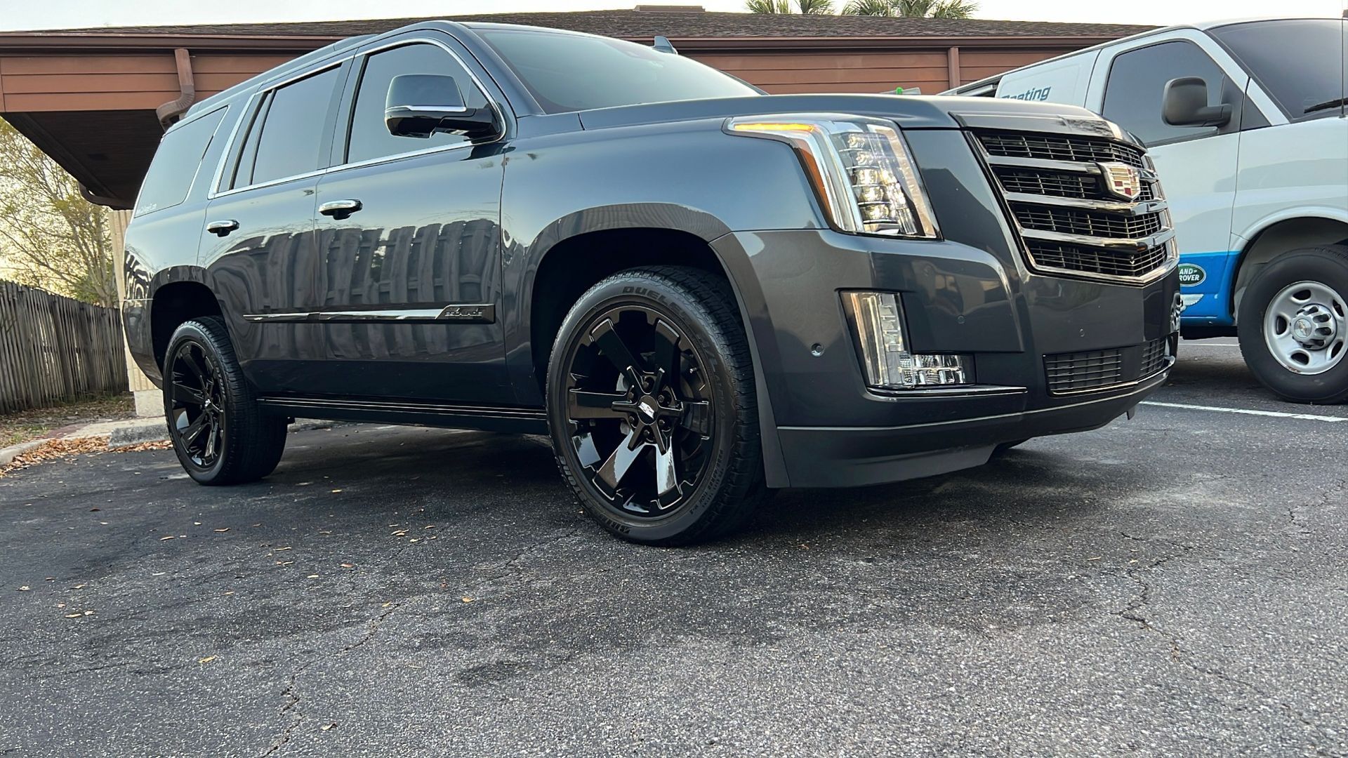 A black cadillac escalade is parked in a parking lot next to a blue van.