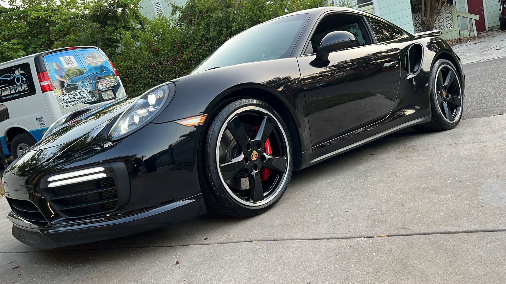 A black porsche 911 turbo s is parked on the side of the road.