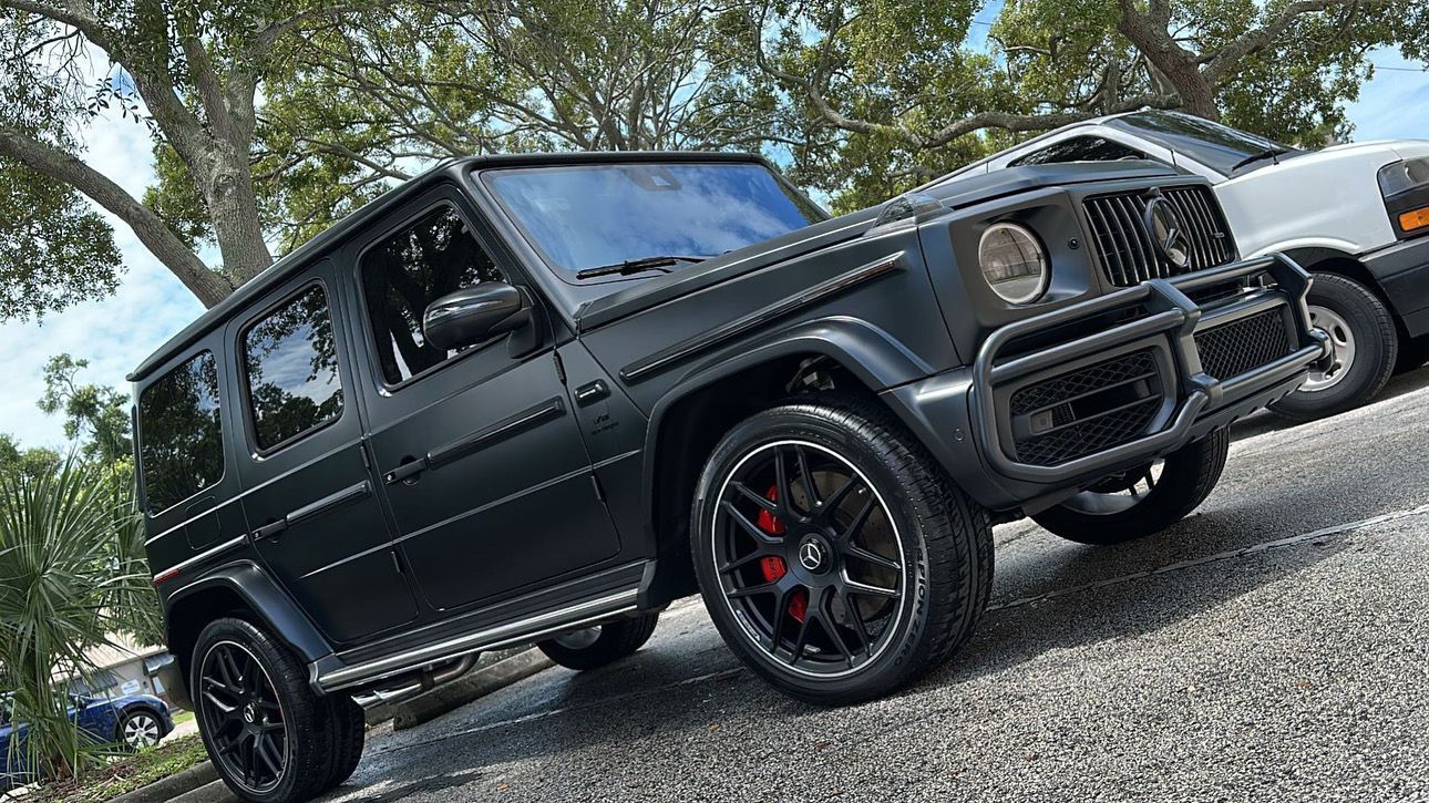 A black mercedes benz g63 is parked on the side of the road.