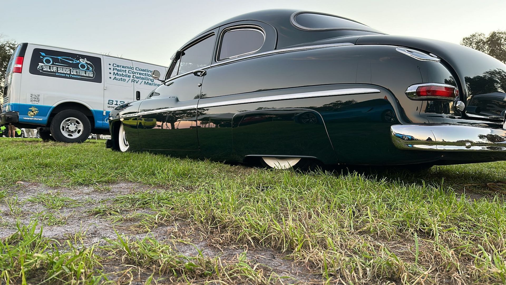A black car is parked in the grass next to a white van.