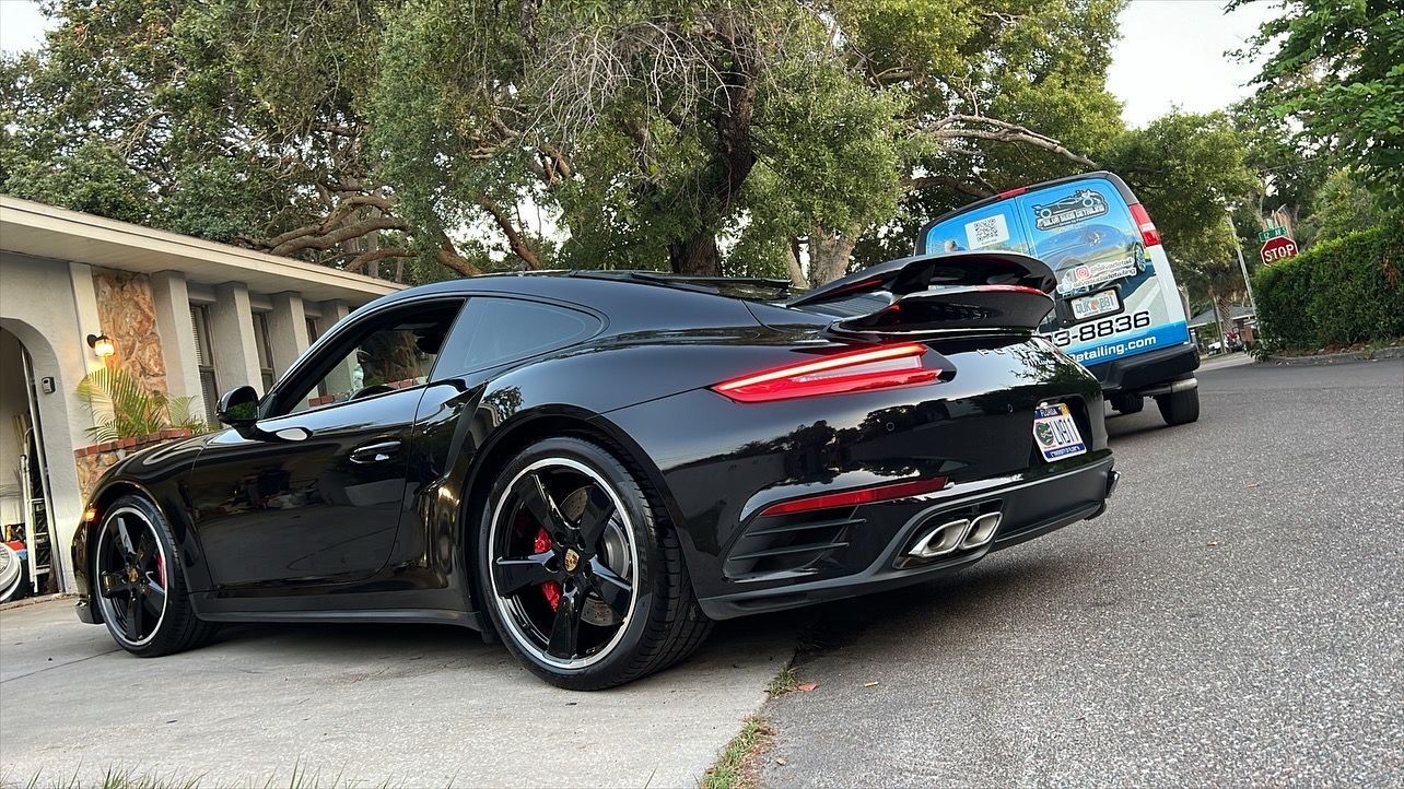 A black sports car is parked on the side of the road in front of a house.