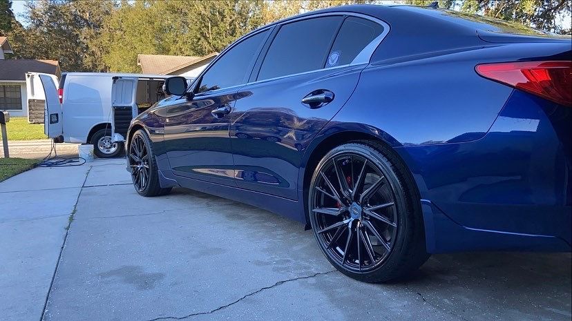 A blue car is parked in a driveway next to a white van.
