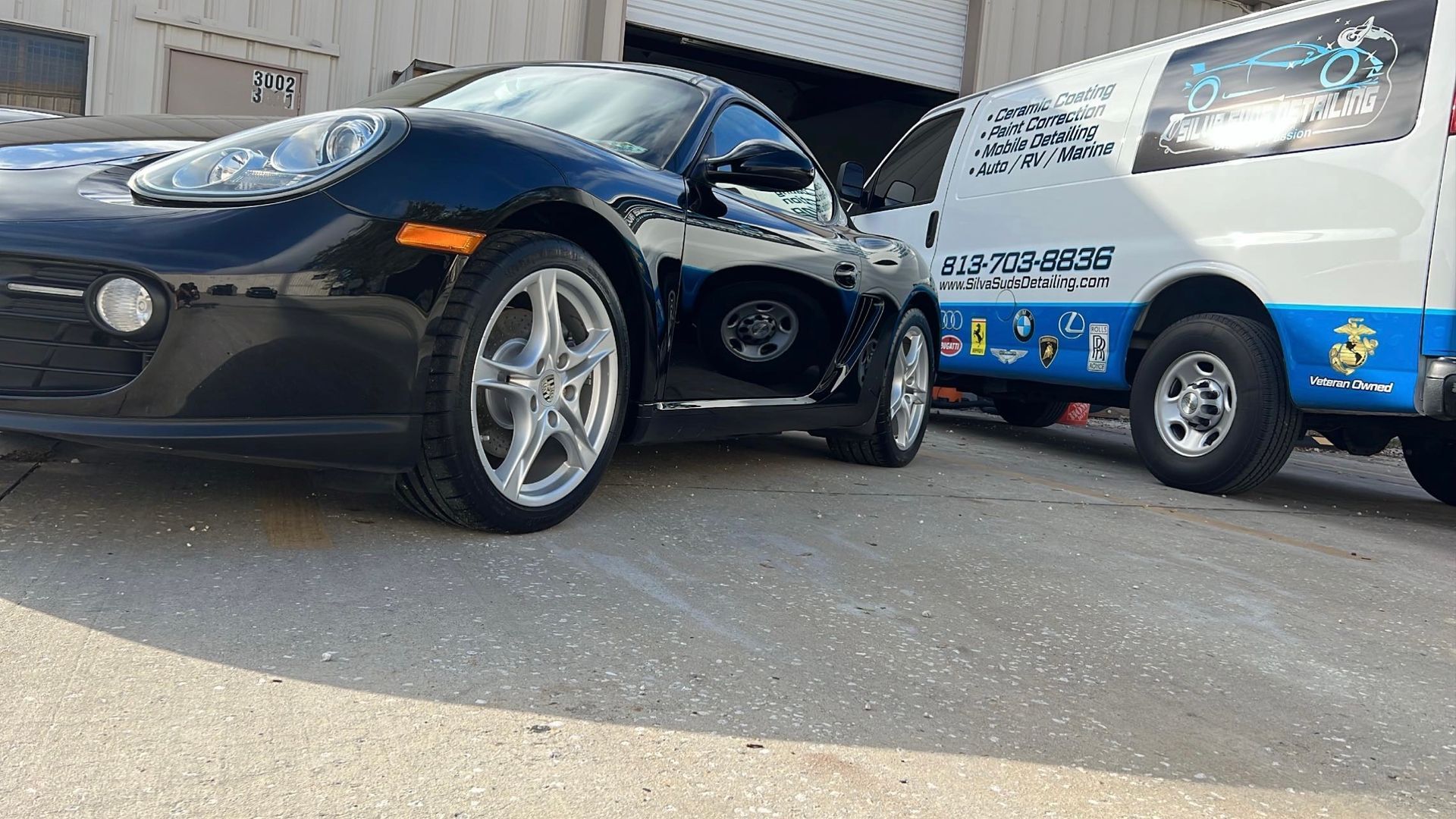 A black sports car is parked next to a white van.