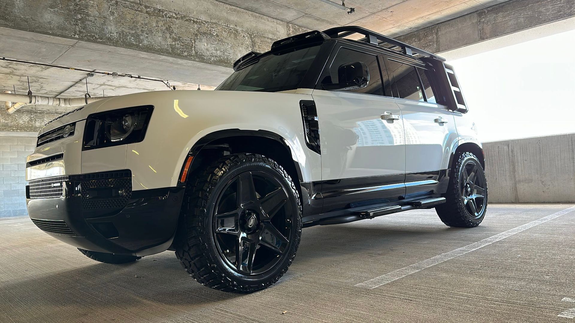 A white land rover defender is parked in a parking garage.