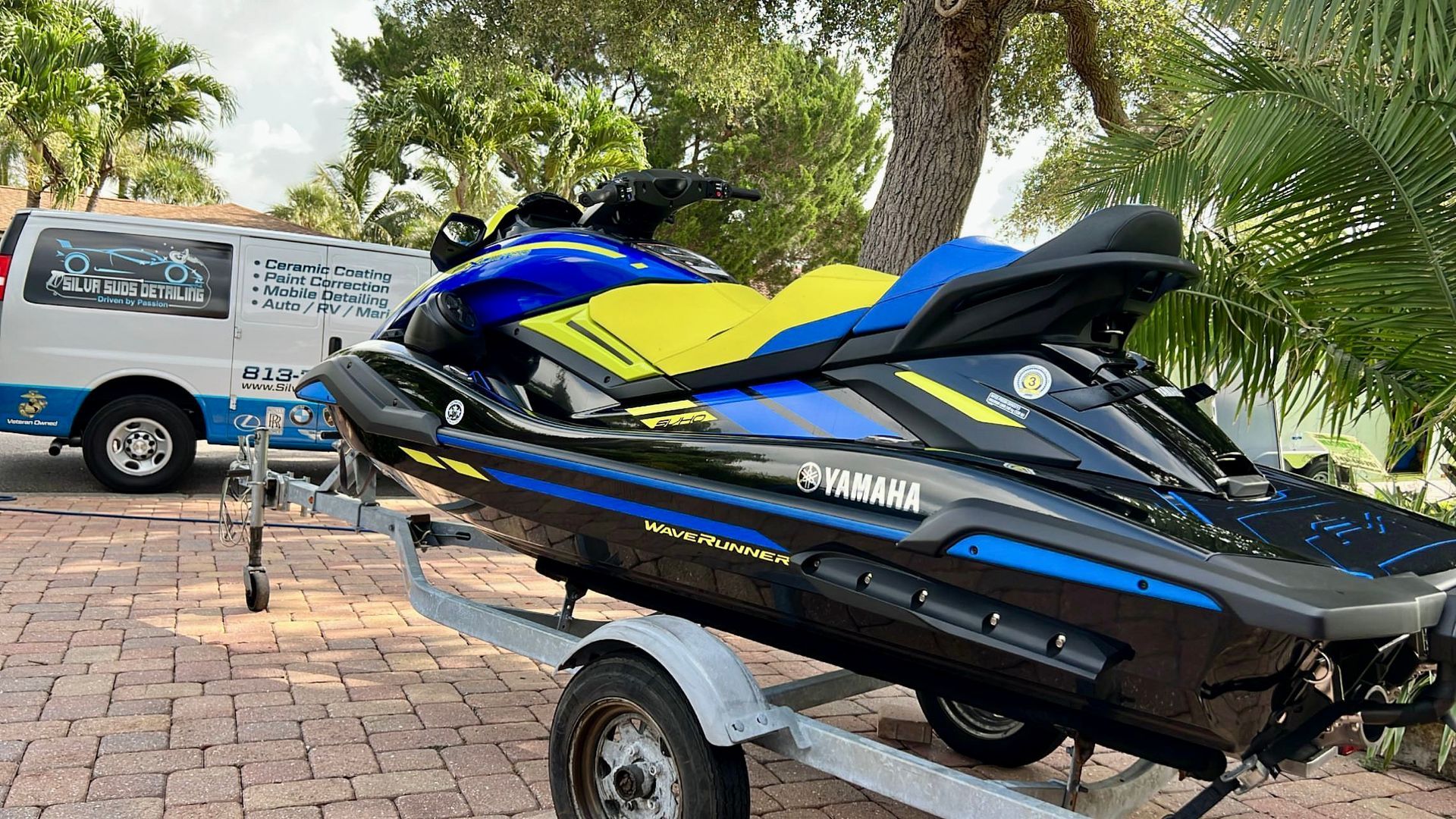 A blue and yellow jet ski is on a trailer next to a van.