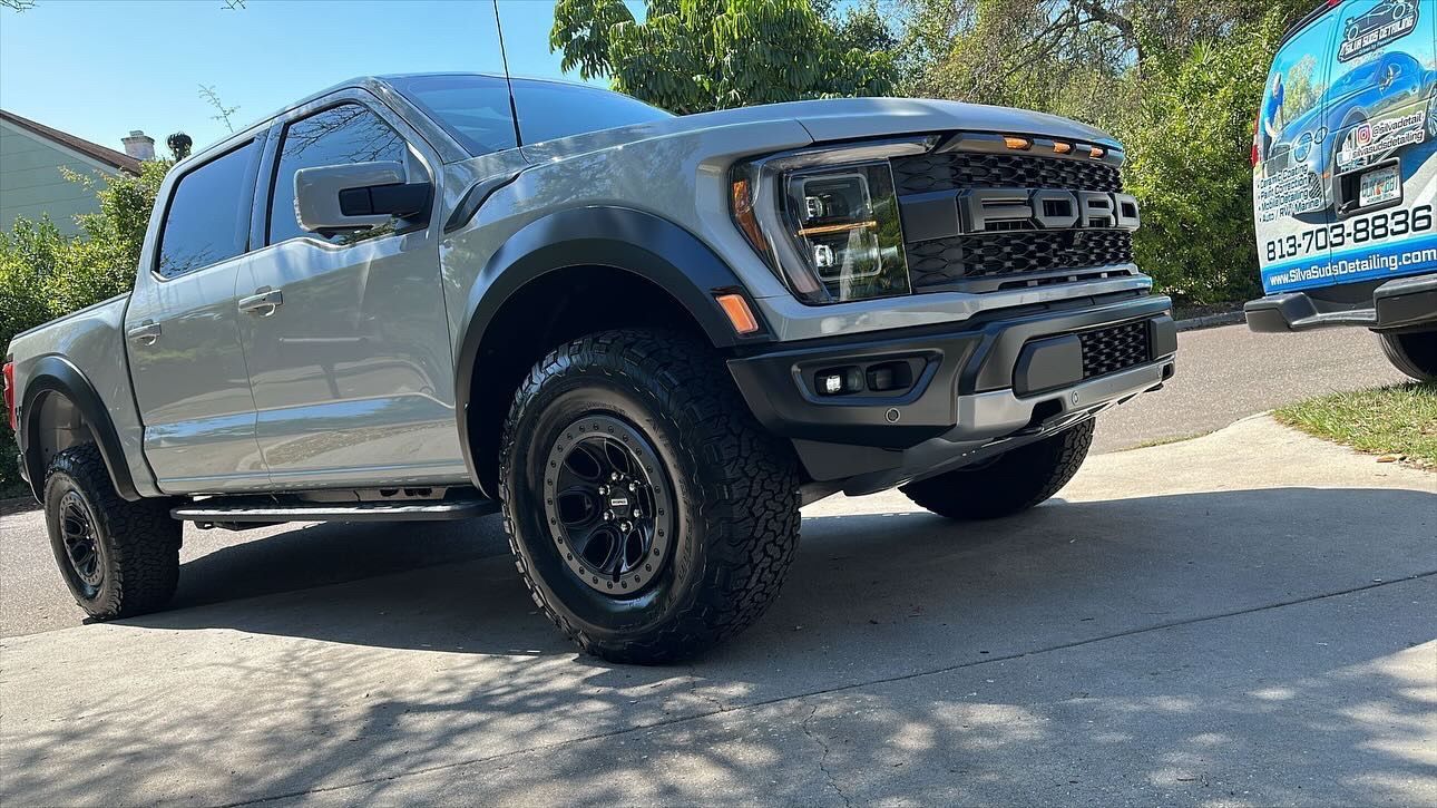A silver ford raptor truck is parked on the side of the road.