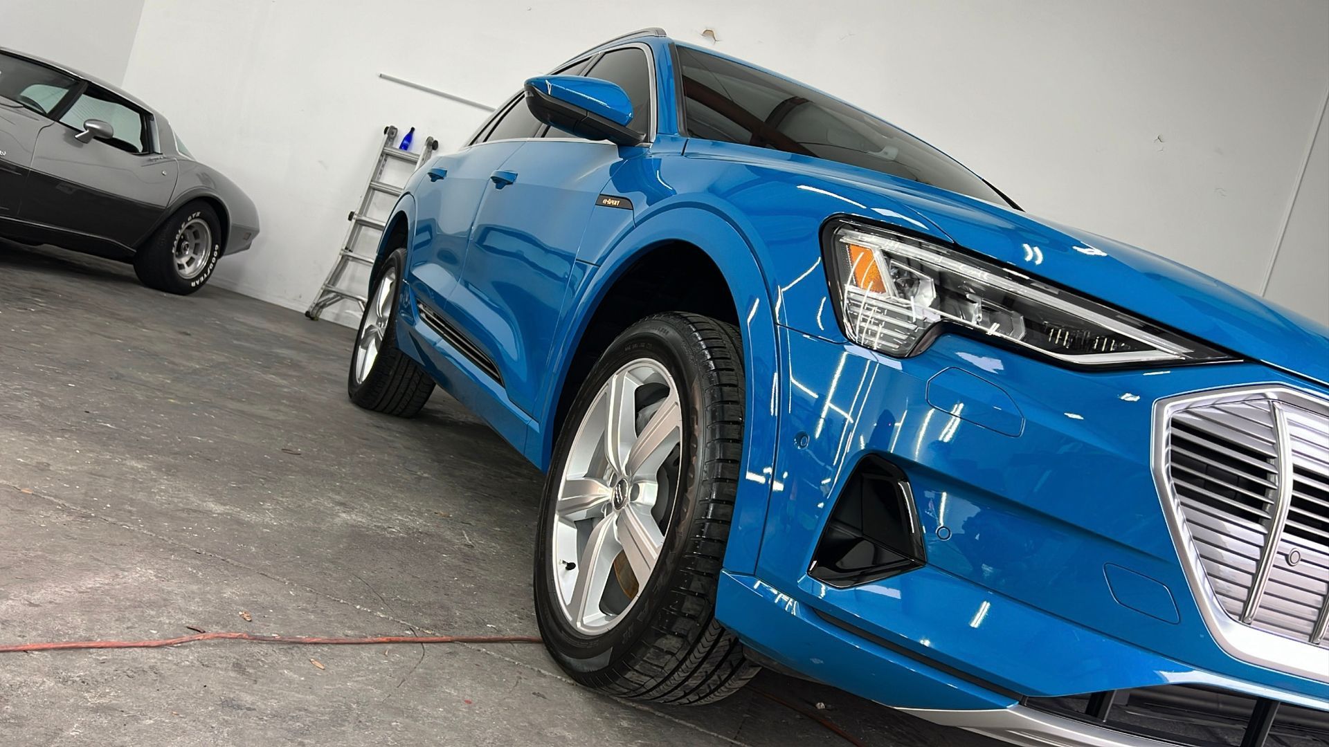 A blue car is parked in a garage next to a black car.