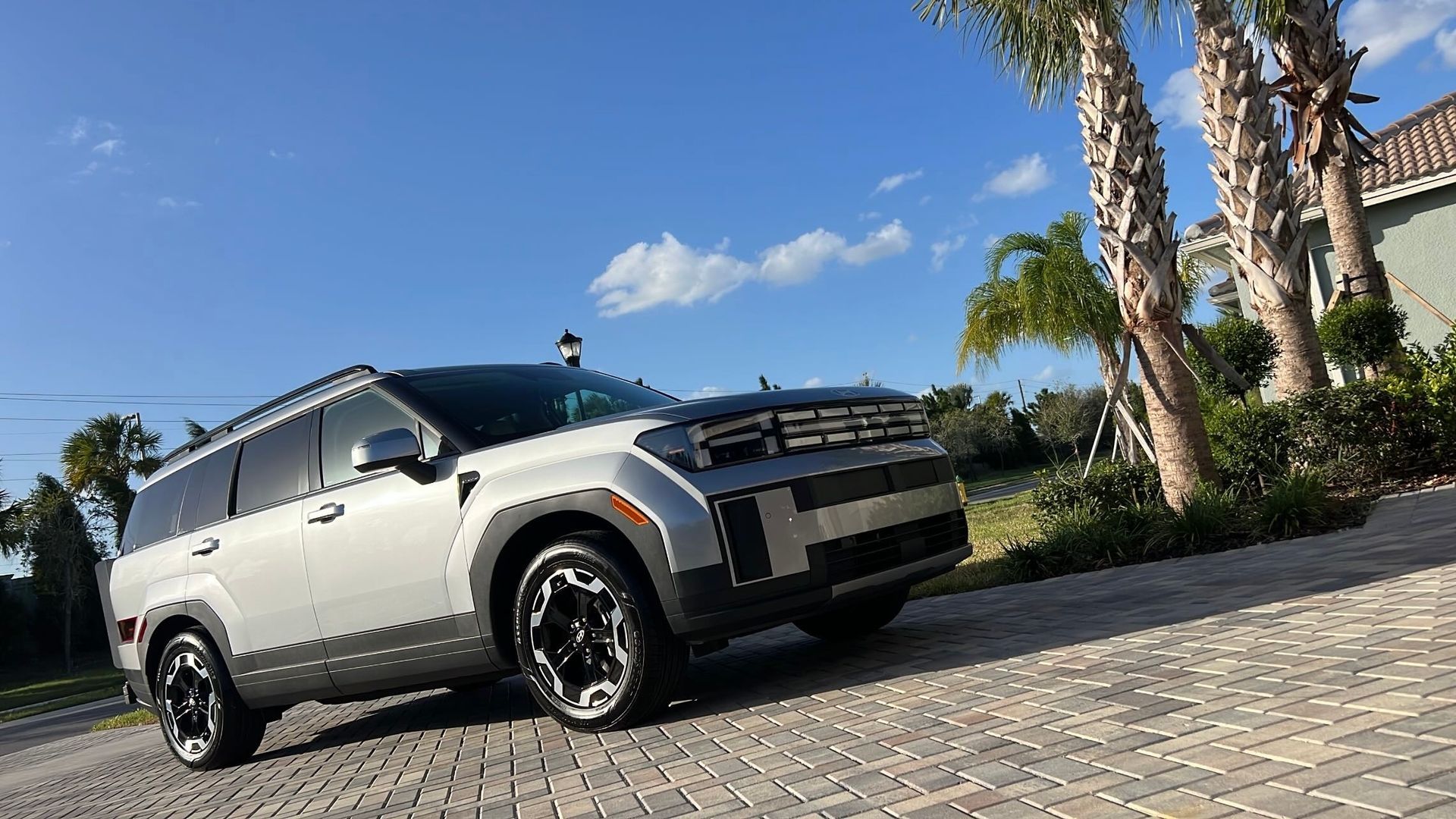 A white suv is parked on a cobblestone driveway next to trees.