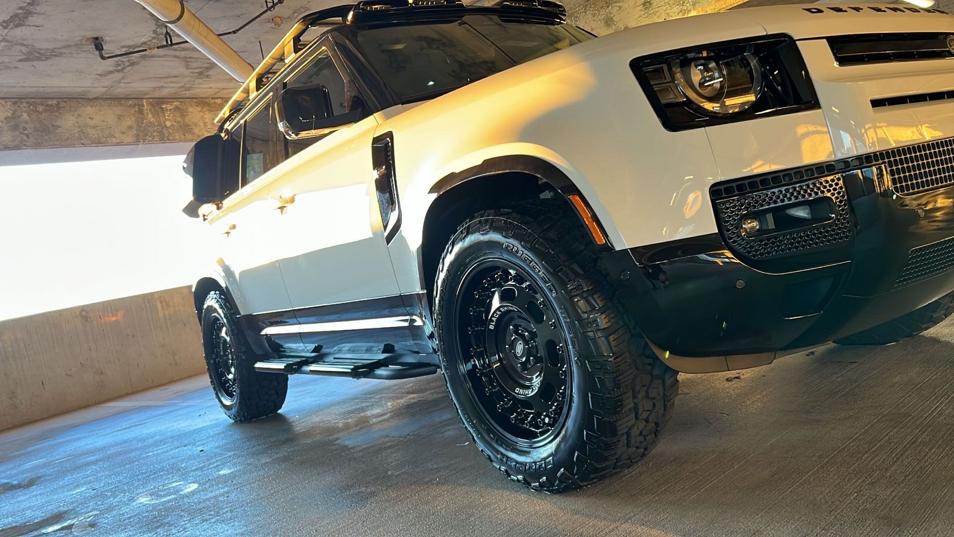 A white suv with black wheels is parked in a parking garage.