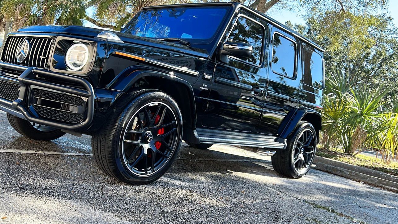 A black mercedes benz g63 amg is parked on a gravel road.