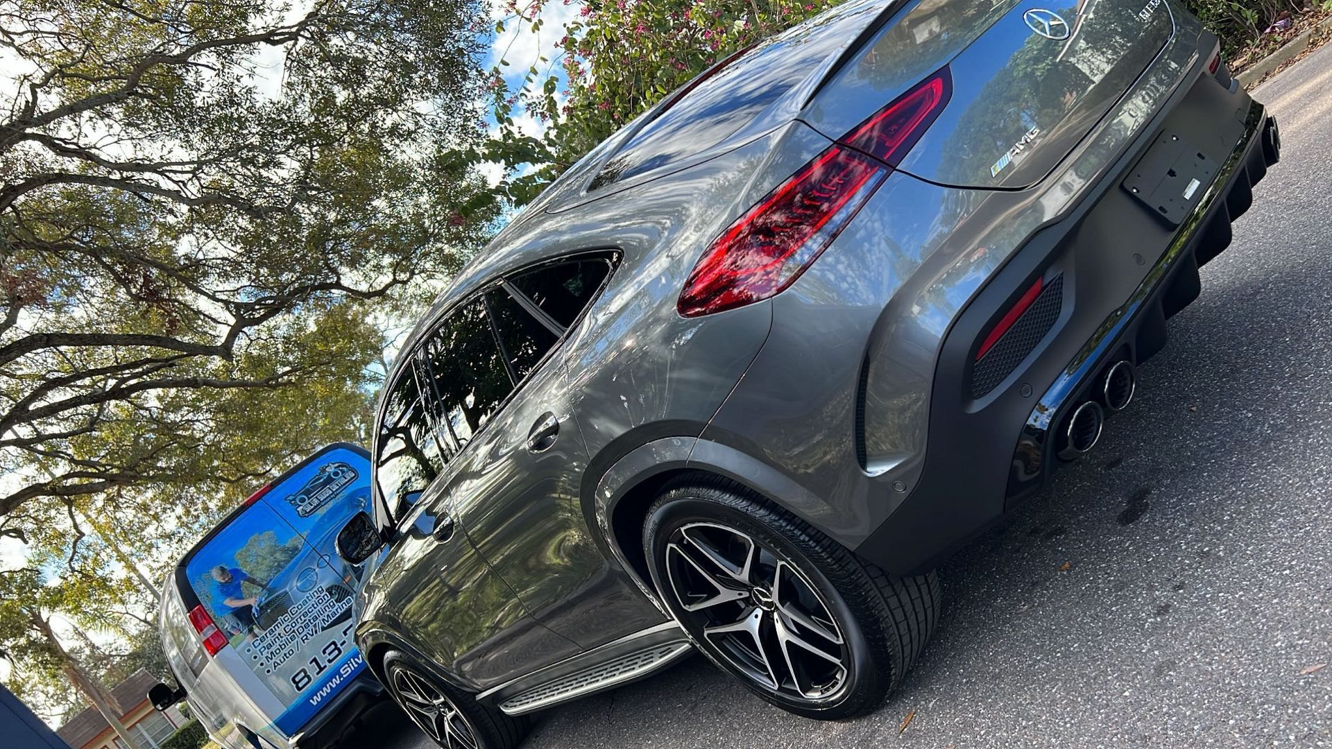 A gray car is parked on the side of the road next to a blue van.