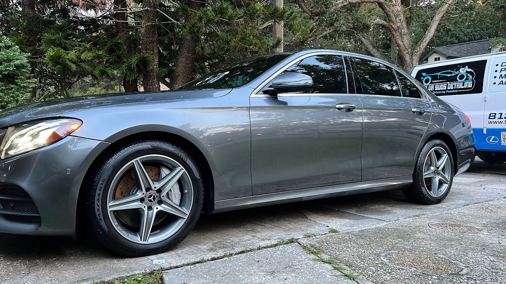 A gray car is parked in a driveway next to a blue van.