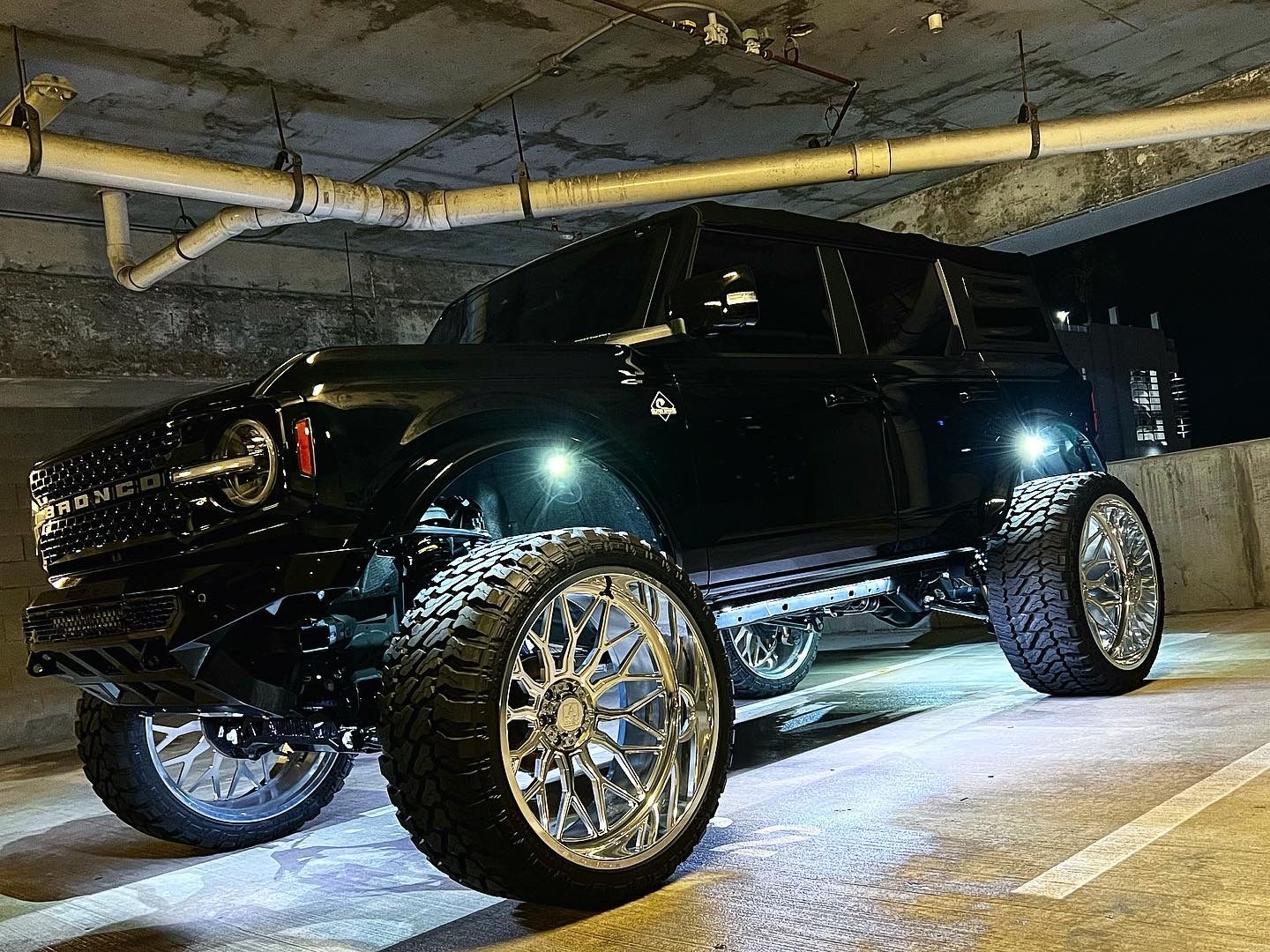 A black ford bronco is parked in a parking garage at night.