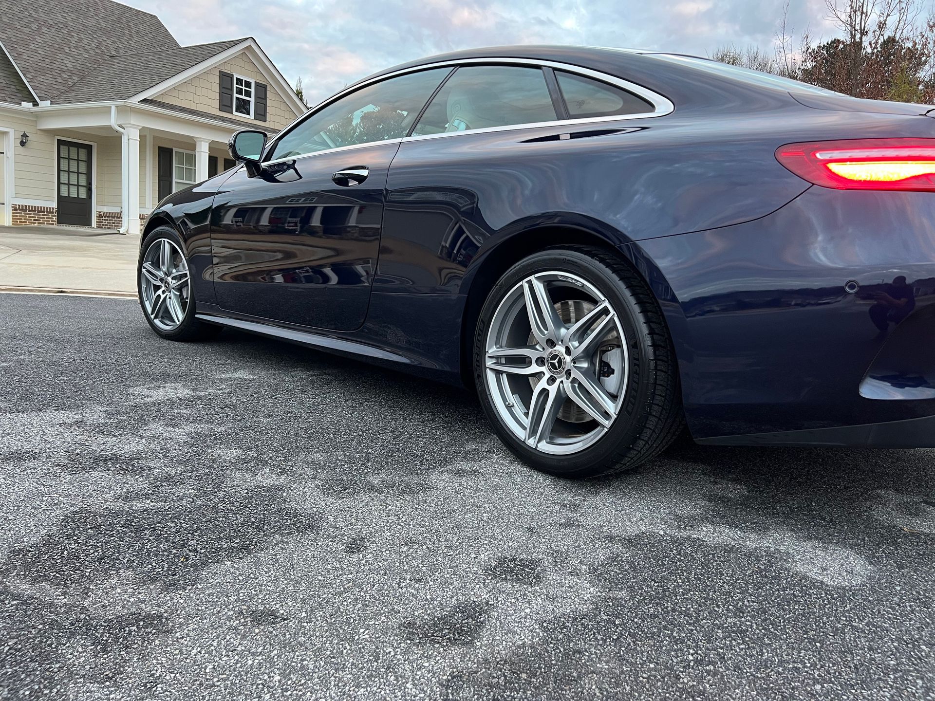 A blue mercedes benz c class coupe is parked in front of a house.