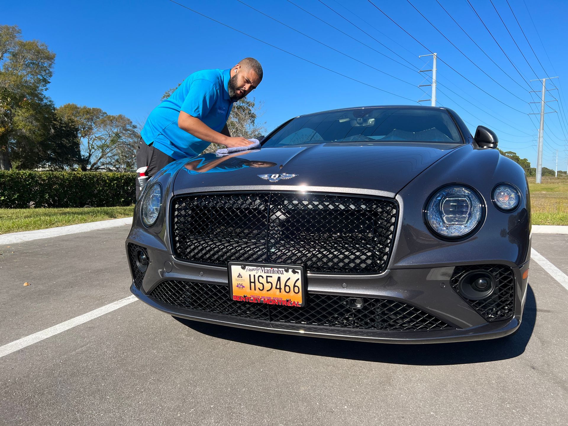 A man is polishing a bentley in a parking lot.
