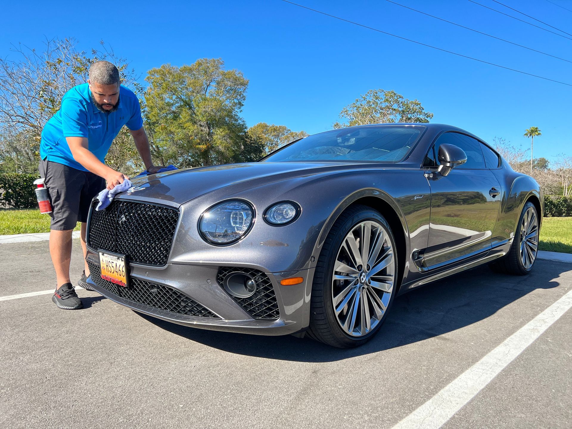 A man is cleaning a bentley in a parking lot.