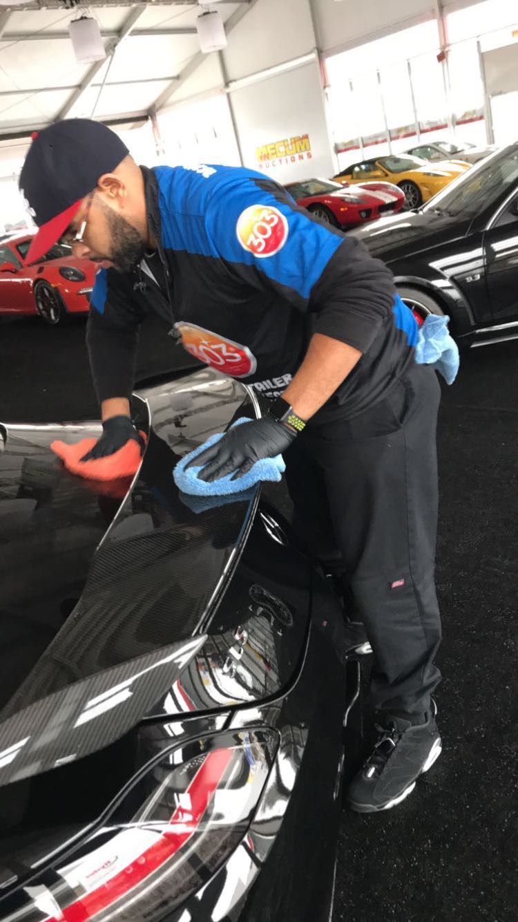 A man is cleaning a car with a cloth in a garage.