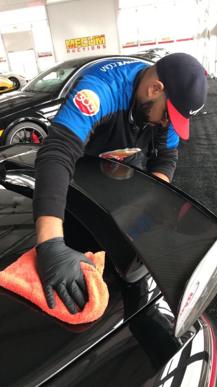A man is cleaning a car with a towel and gloves.
