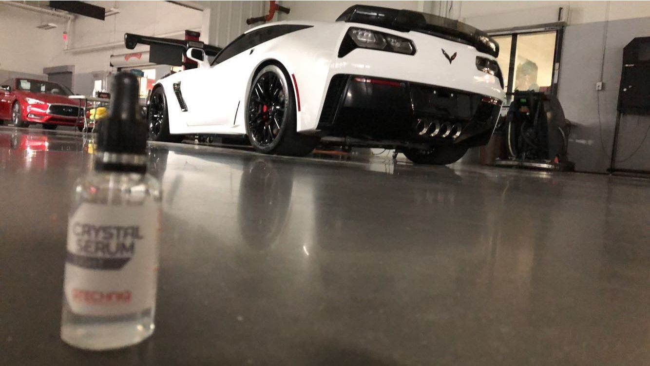 A white corvette is parked in a garage next to a bottle of polish.