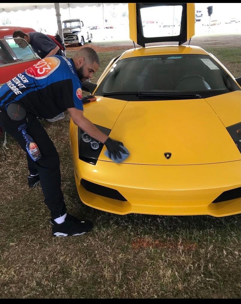 A man is cleaning a yellow sports car with a cloth