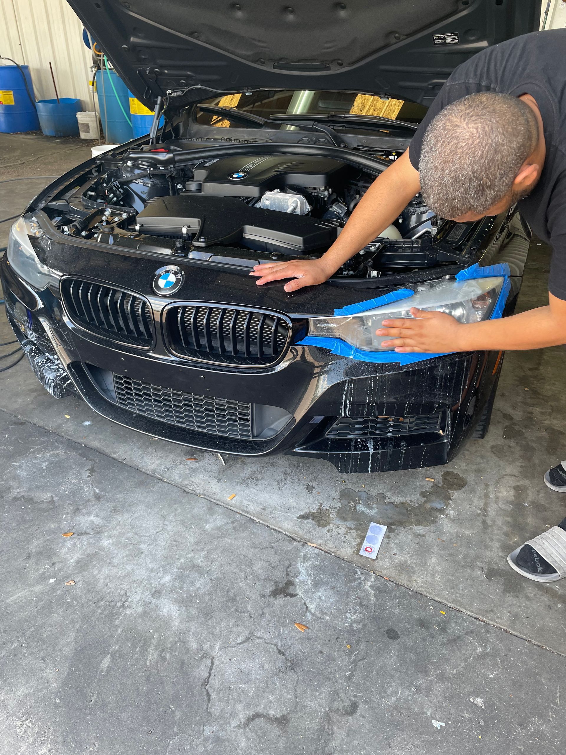 A man is cleaning the front of a bmw with a blue tape.