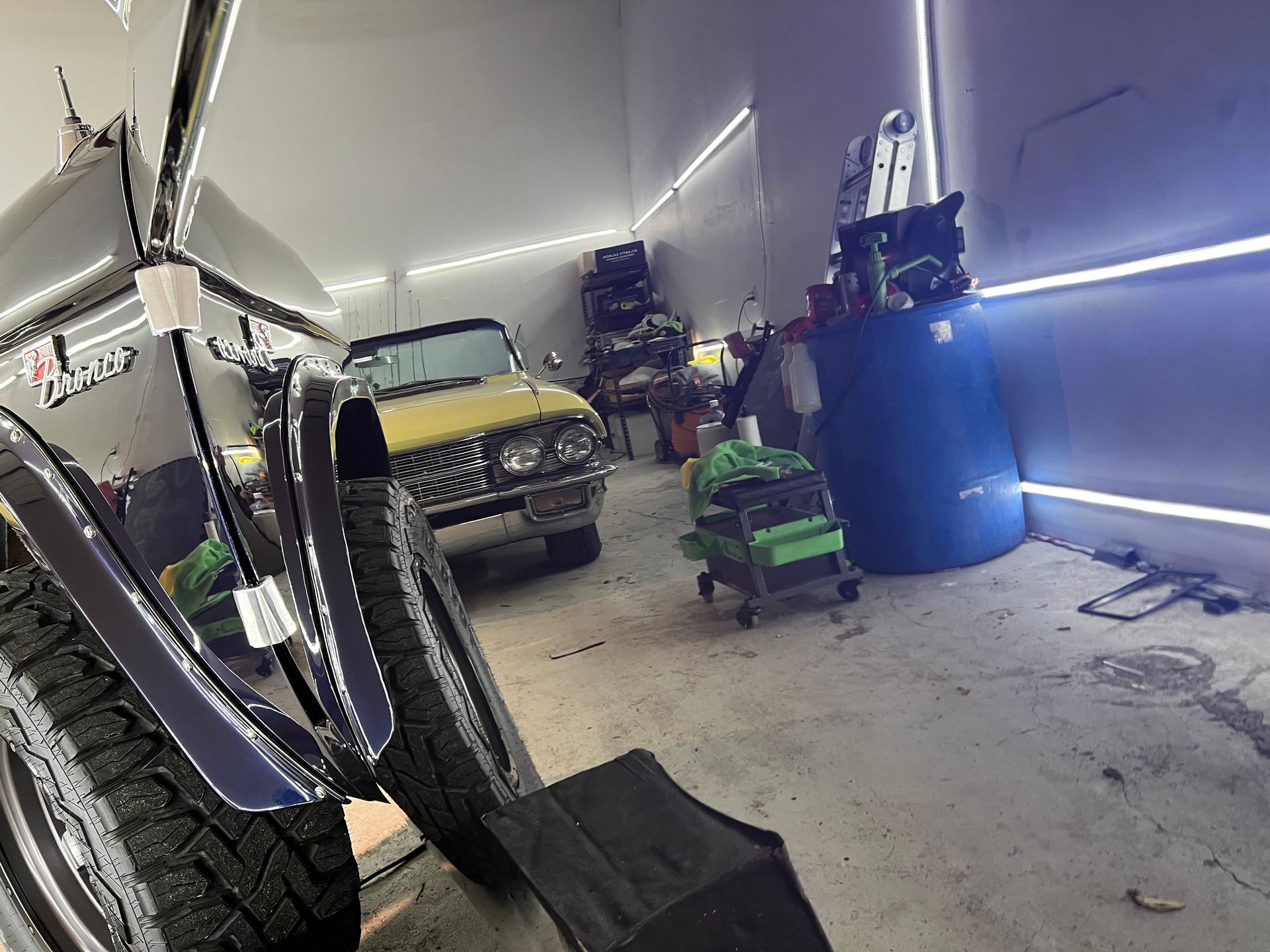 A jeep is parked in a garage next to a yellow car.