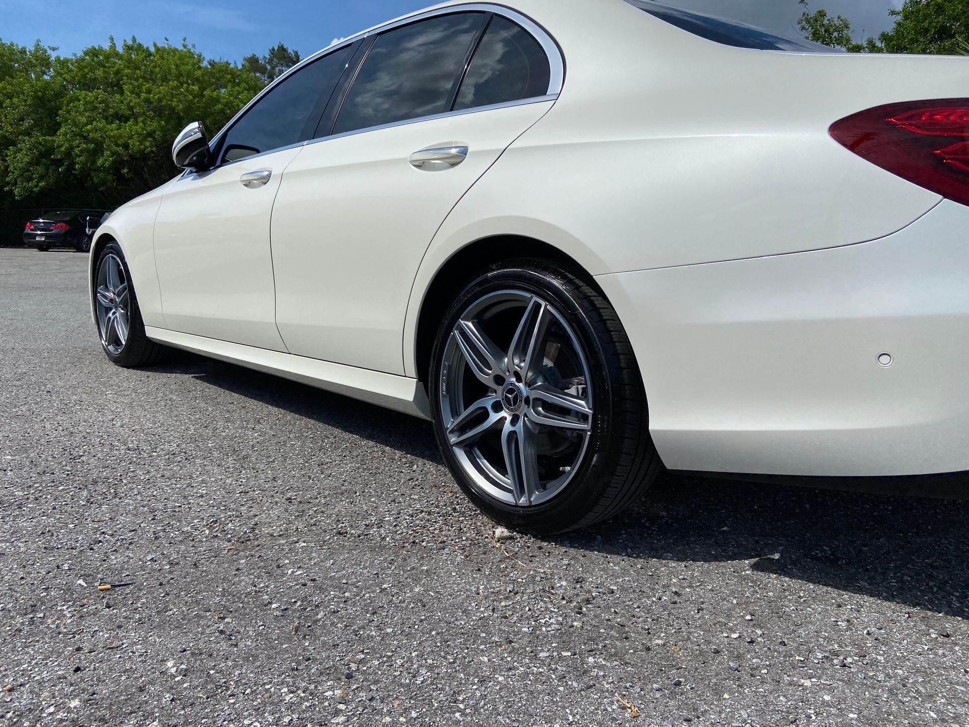 A white mercedes benz is parked in a gravel lot.