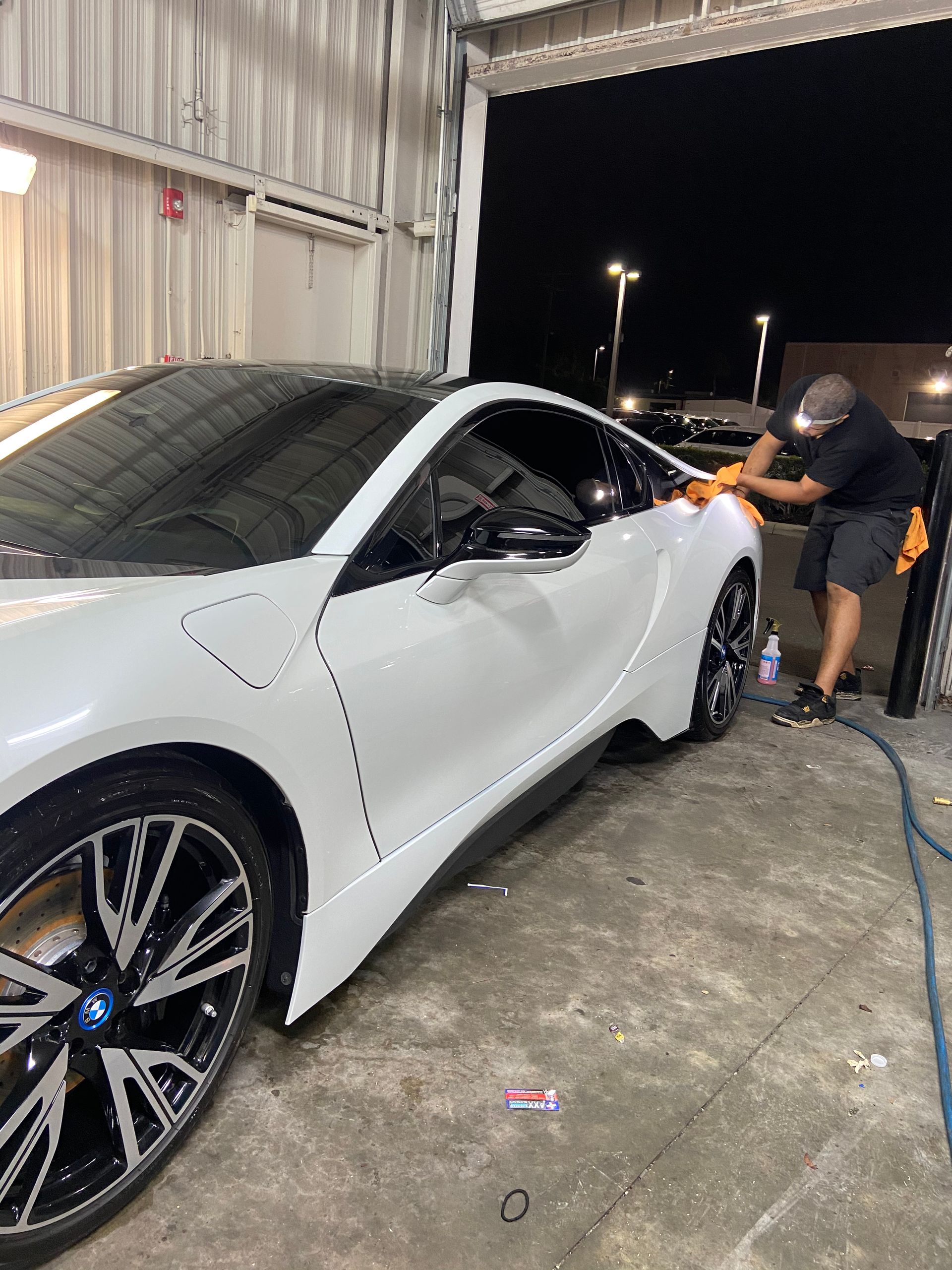 A man is polishing a white sports car in a garage.