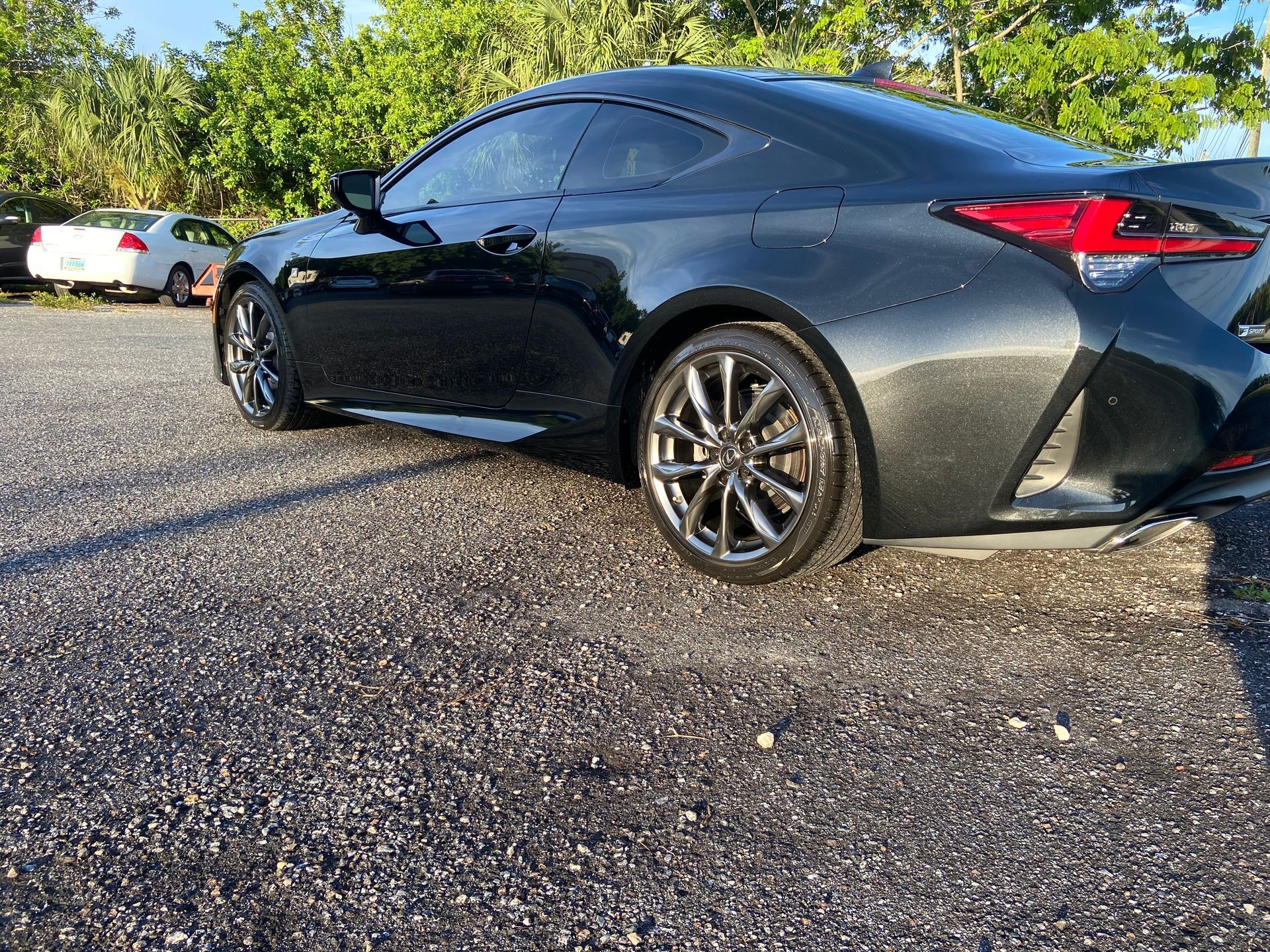 A black sports car is parked in a gravel lot.