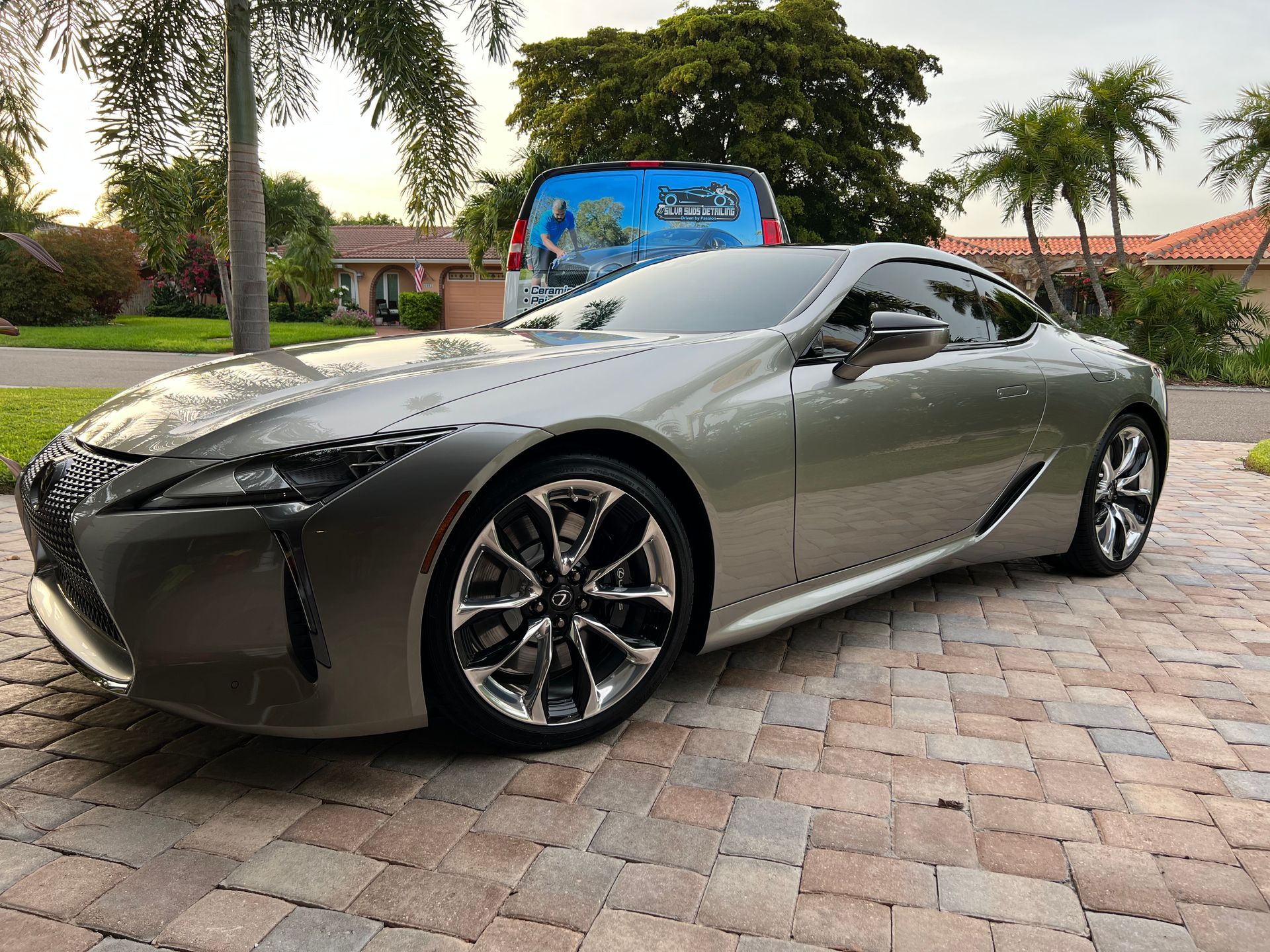 A silver sports car is parked on a brick driveway in front of a house.