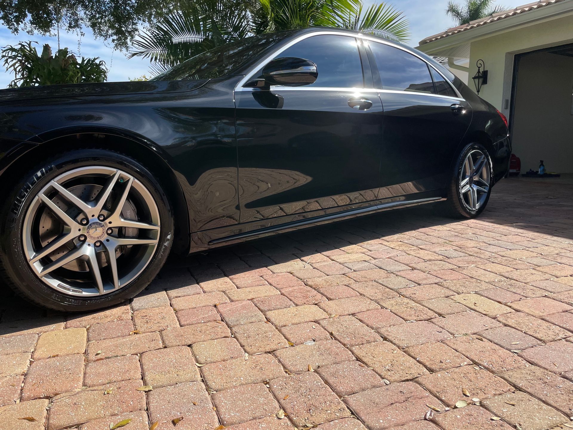 A black car is parked on a brick driveway in front of a garage.