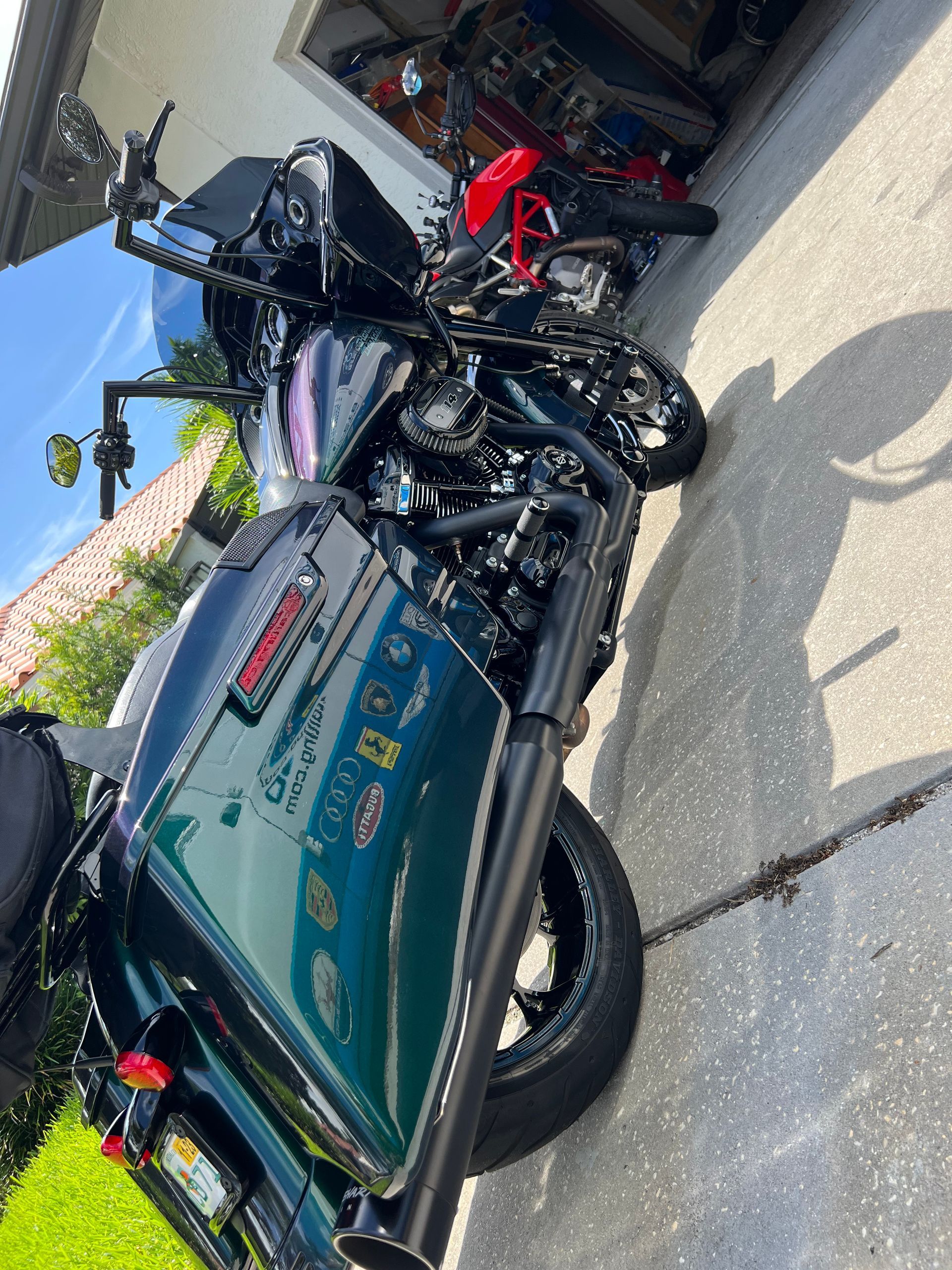 A green harley davidson motorcycle is parked on the sidewalk in front of a garage.