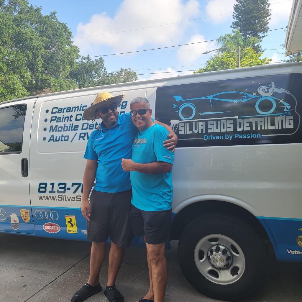 Two men are posing in front of a van that says silva suds detailing
