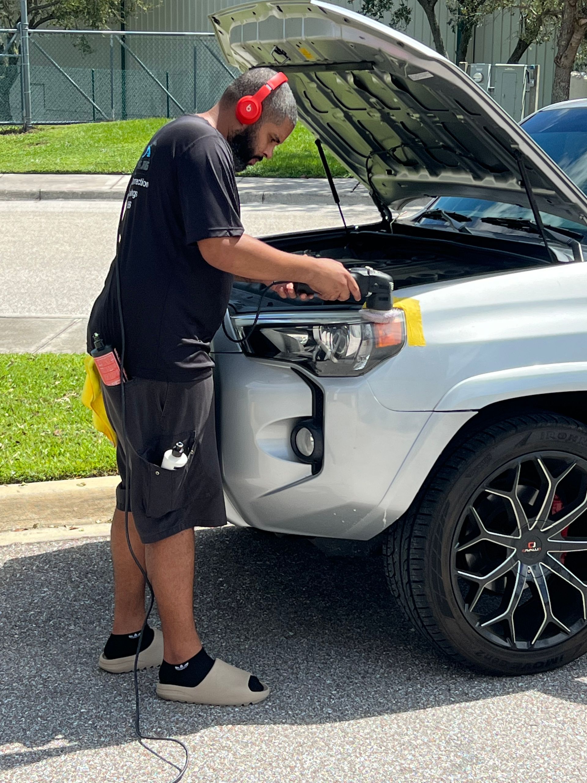 A man wearing headphones is working on a car with the hood open.