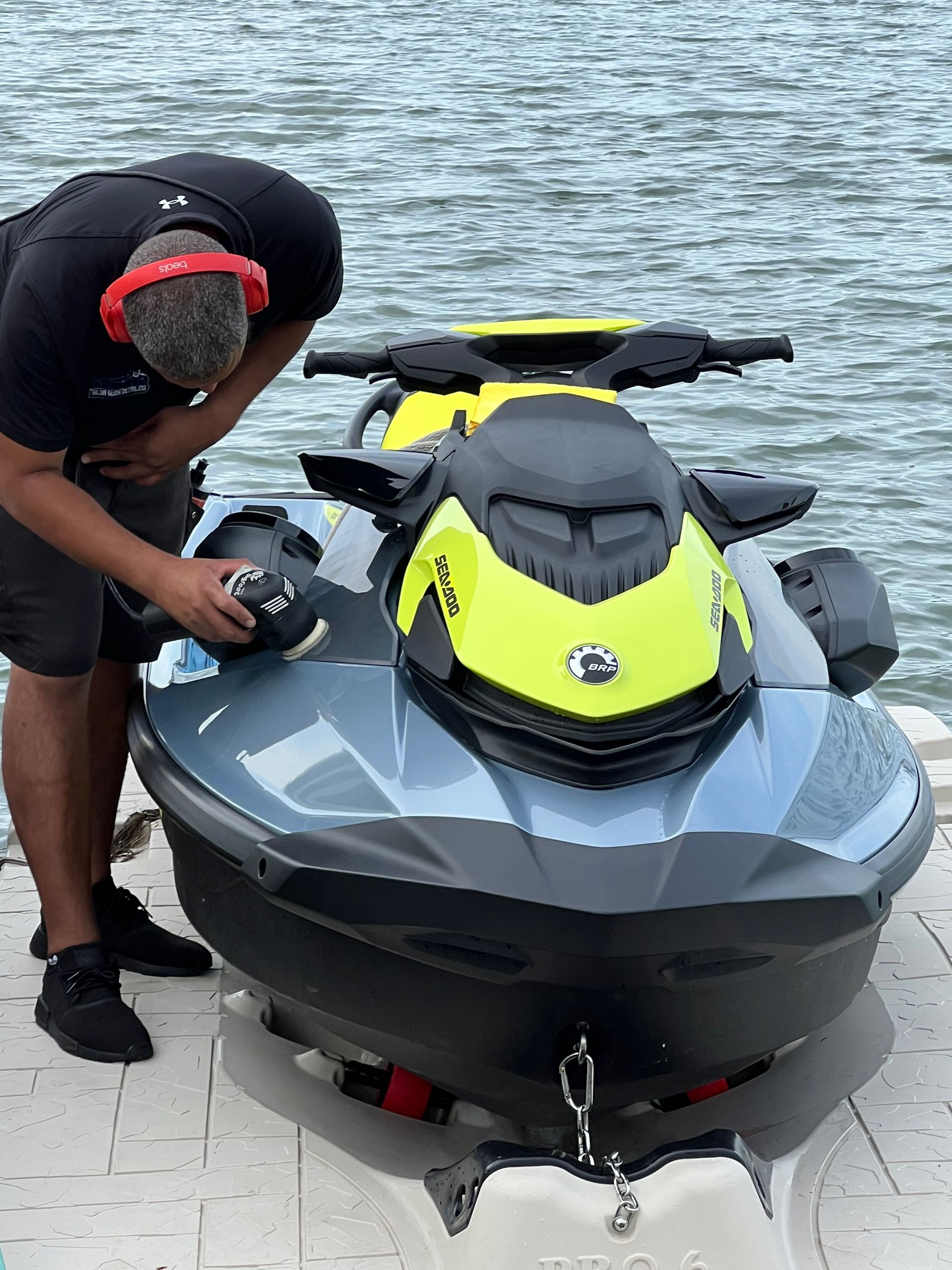 A man is polishing a jet ski on a dock near the water.