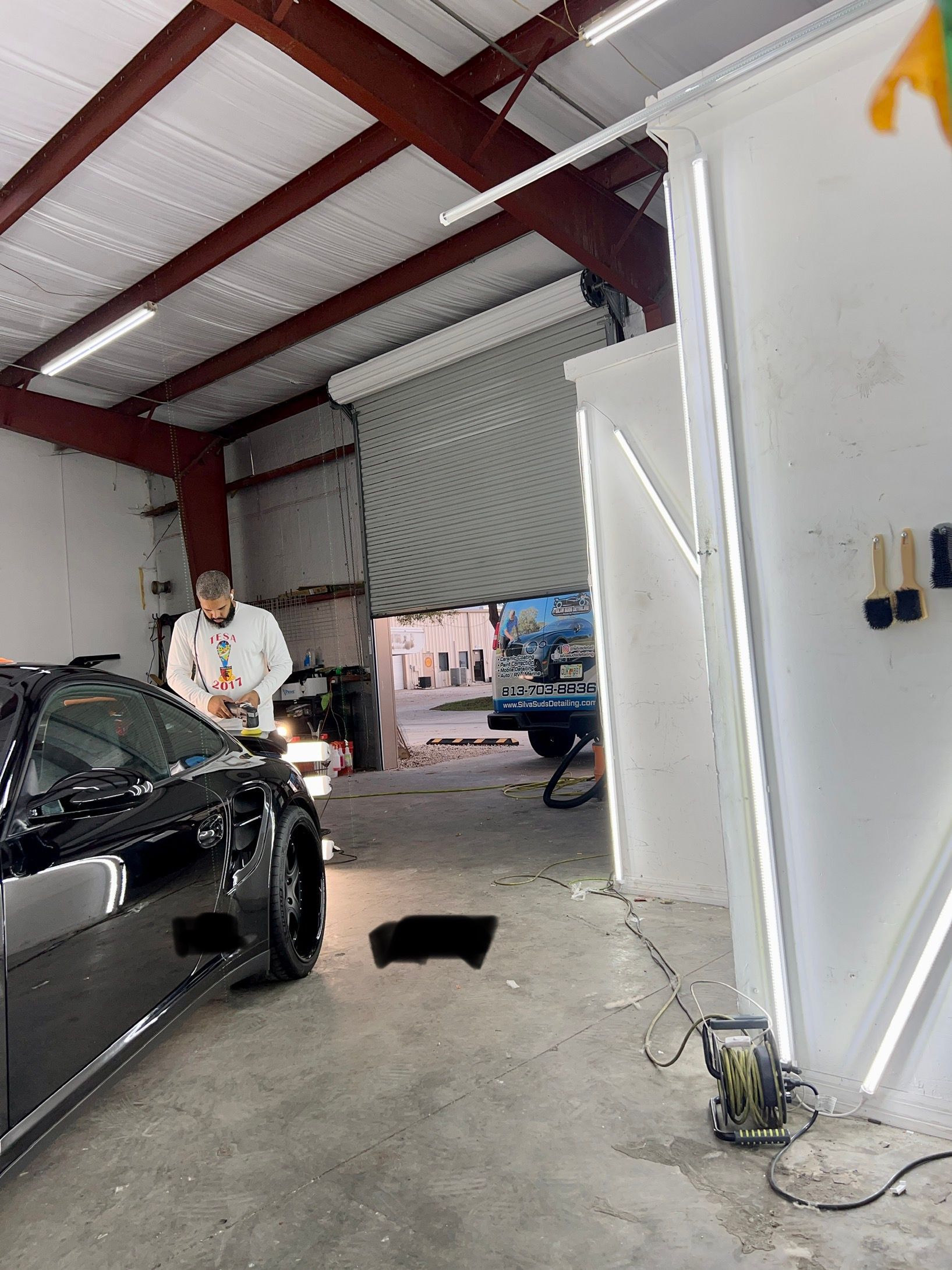 A man is polishing a black car in a garage.