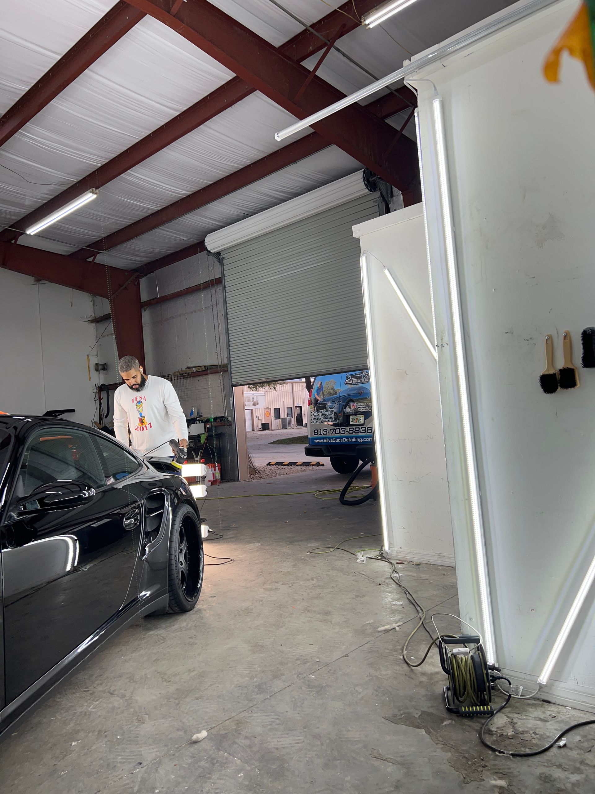 A man is standing next to a black car in a garage.