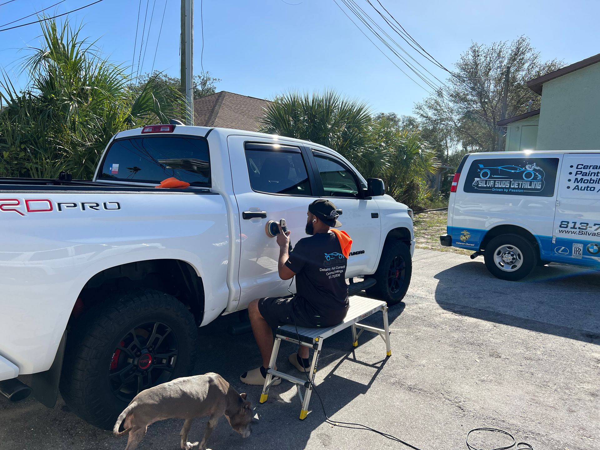 A man is sitting on a stool next to a white truck.
