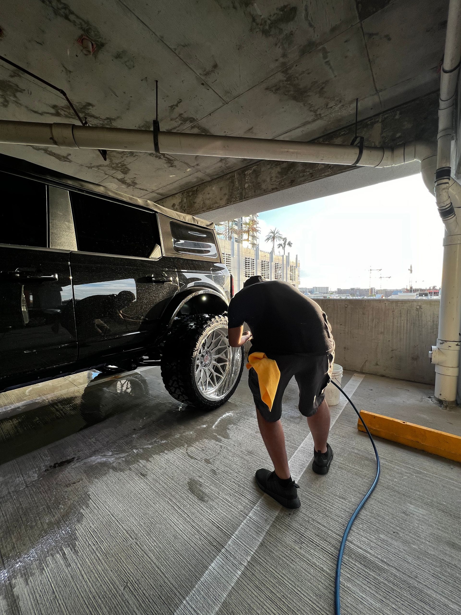 A man is washing a black truck in a parking garage.