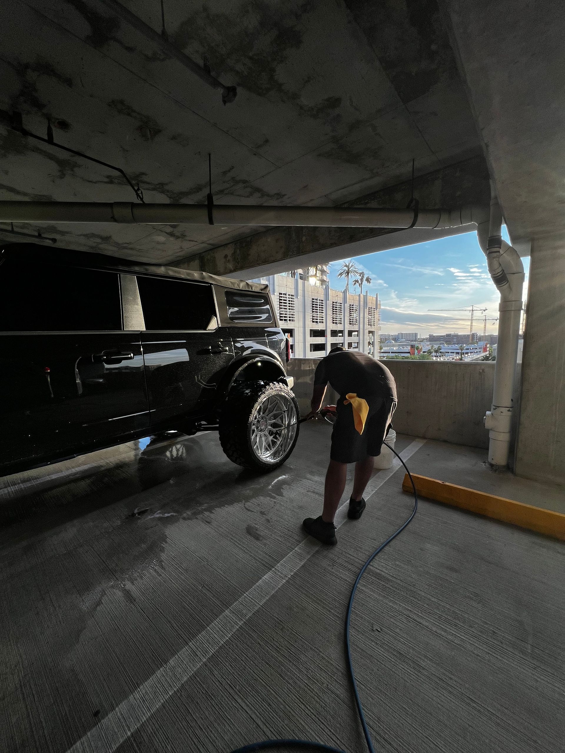 A man is washing a black truck in a parking garage.